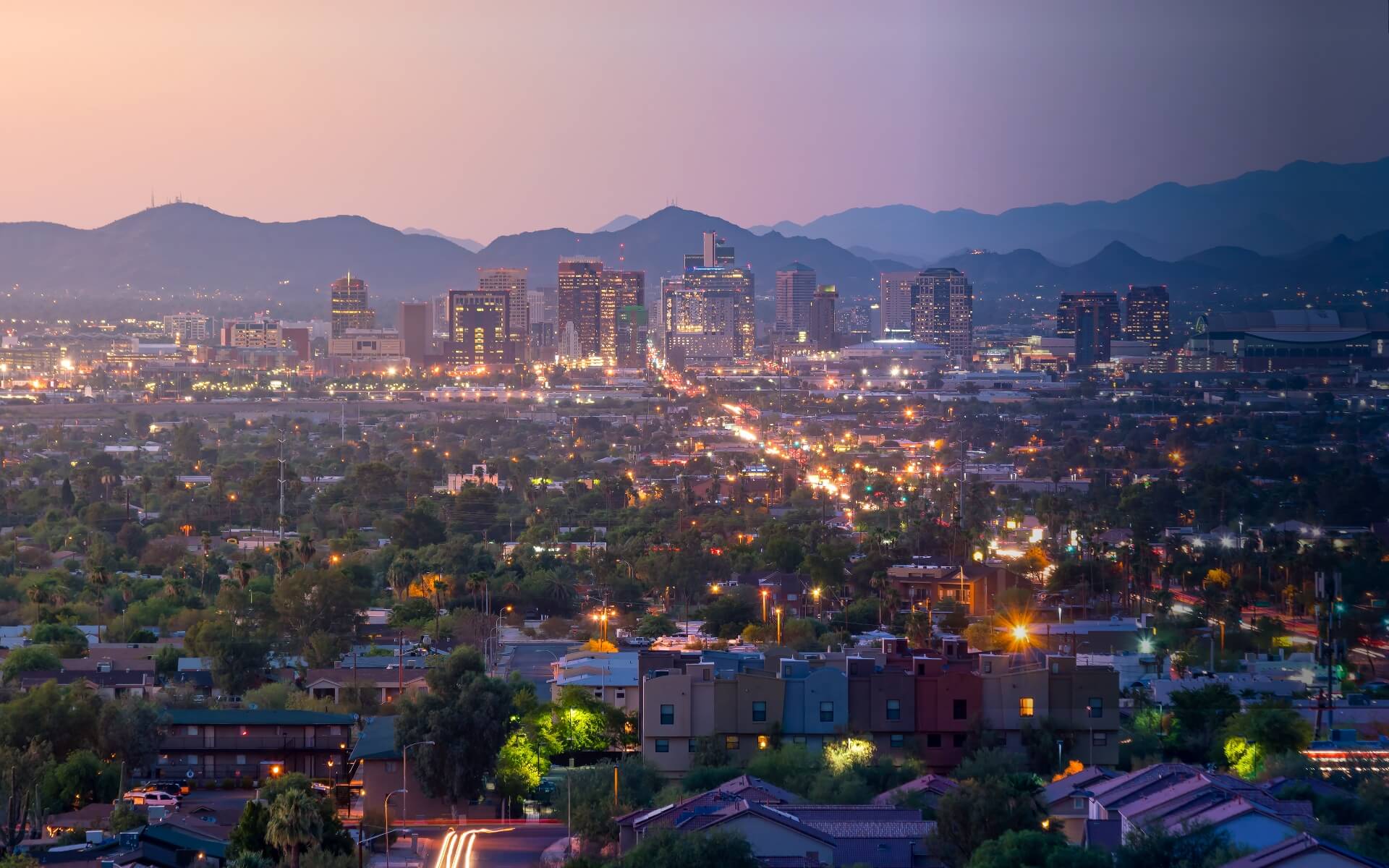 A cityscape at dusk with mountains in the background.
