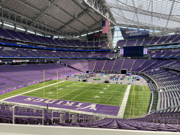 The interior view of U.S. Bank Stadium Field, an event site of ACP's CLEANPOWER 2024 conference. This image shows the entirety of the stadium, including the field and thousands of purple bleacher seats.